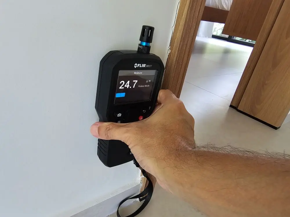 Inspeção técnica com medidor de umidade FLIR MR277 em modo não invasivo (pinless), verificando a presença de umidade ascendente na parede junto ao piso.